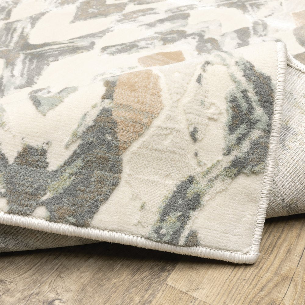 Abstract-pattern rug in cream, beige and gray-blue hues with a soft pile and rolled edge on a wooden floor.