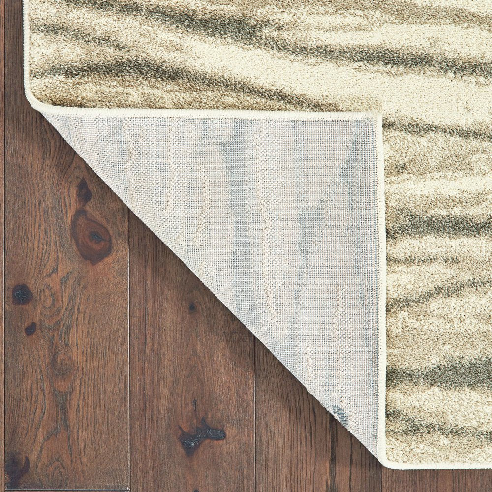 Beige textured area rug with wavy darker stripes, partially flipped at corner to reveal gray underside on dark wood floor.