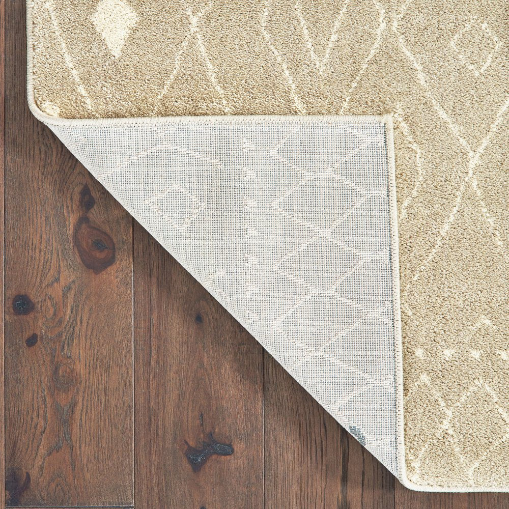 Beige area rug with white geometric pattern, folded corner reveals gray backing on dark wood floor.