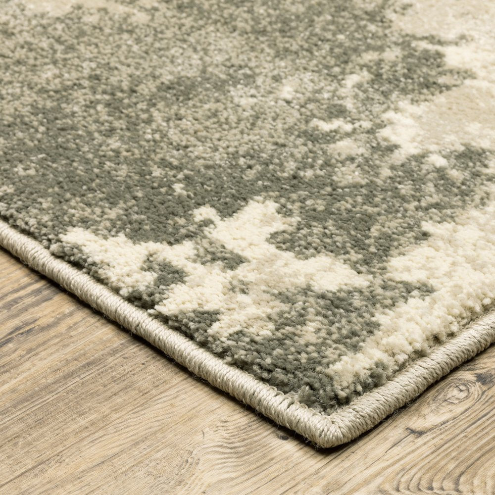 Close-up of gray and cream plush patterned area rug with beige binding on wood floor.