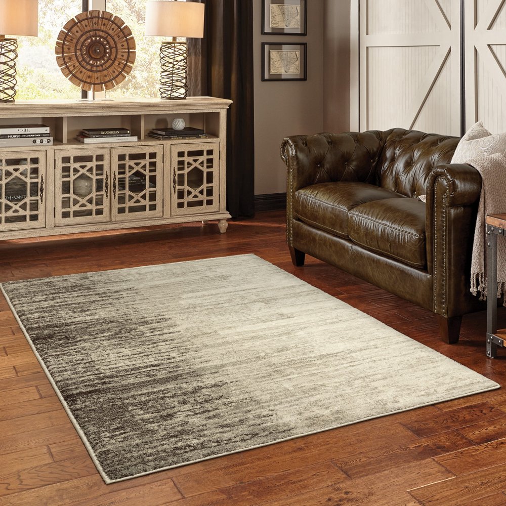 Rectangular gray gradient low-pile area rug in a modern transitional living room with a brown leather sofa.