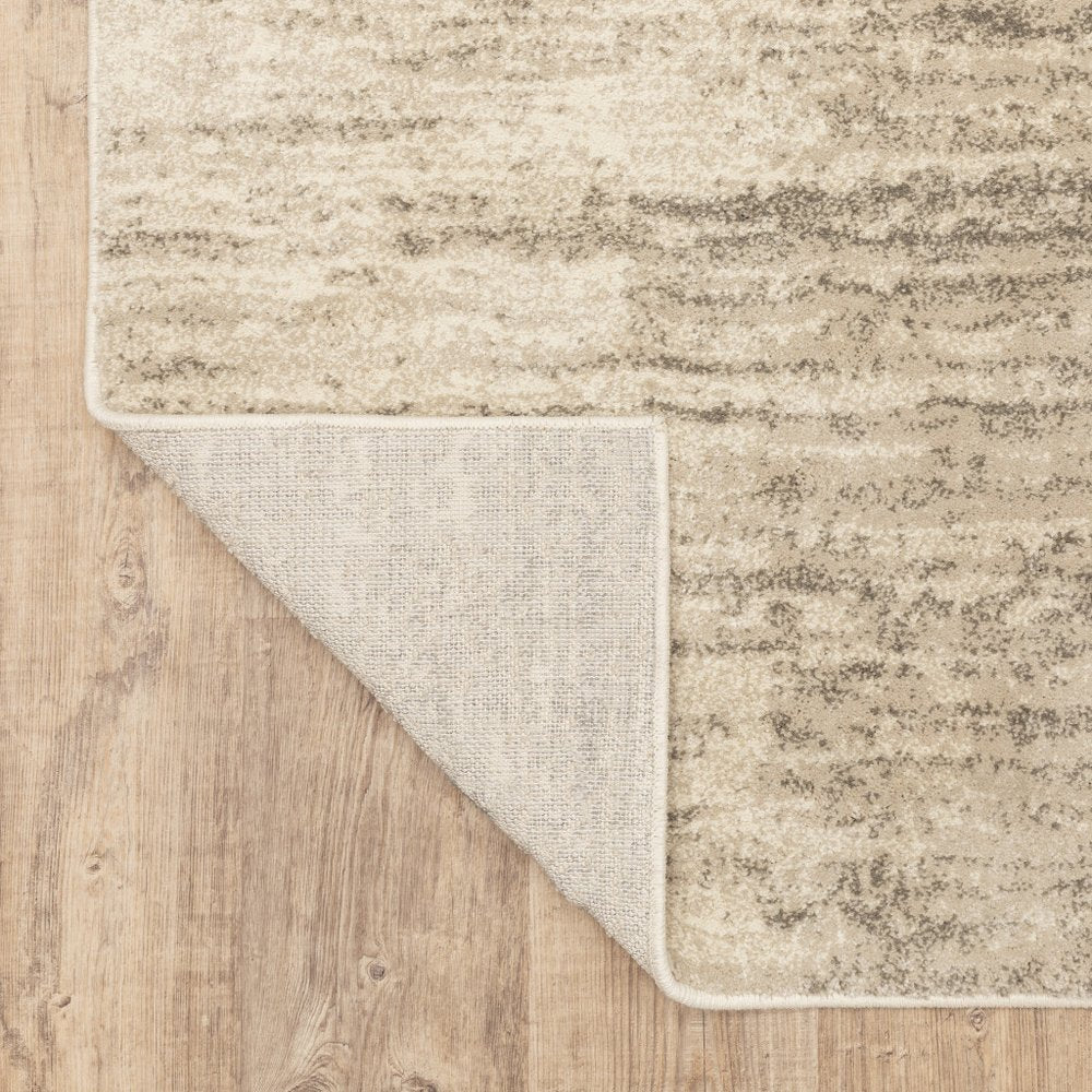 Cream and gray marbled area rug with light border, partially folded to show underside on wooden floor.