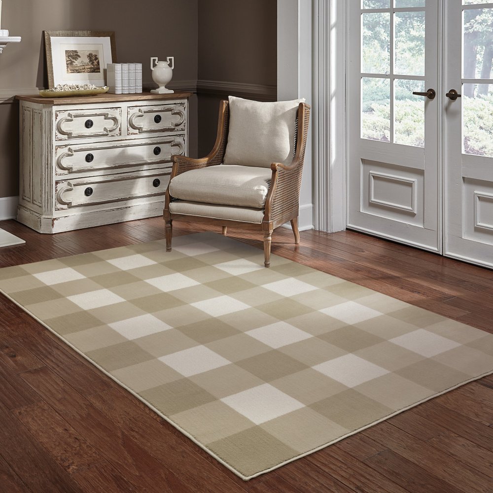 Beige and ivory geometric area rug in a cozy living room with a wicker-backed armchair and distressed white dresser.