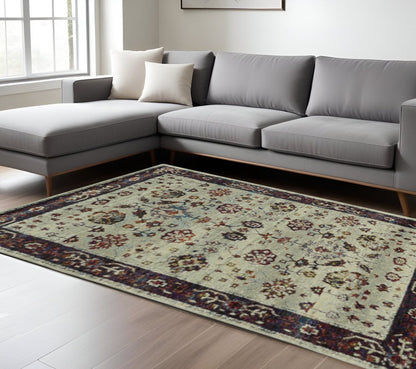 Modern gray L-shaped sectional sofa with light wood legs, beige pillows, and a cream oriental rug with blue and rust border.