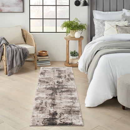 Long neutral runner rug with a distressed abstract pattern in beige, taupe and charcoal beside a bed in a modern bedroom.