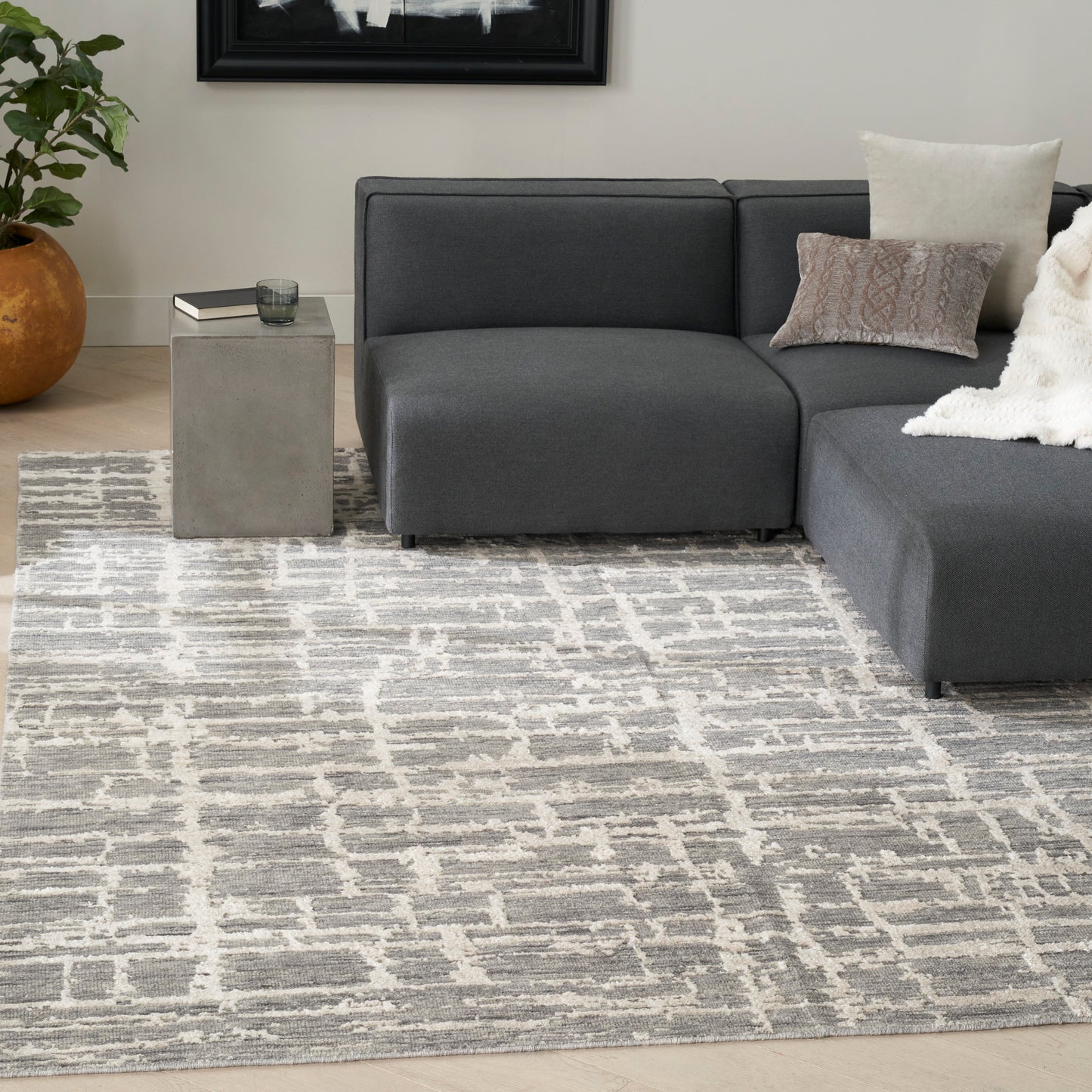Cream geometric rug in a living room with a charcoal gray sectional with chaise, a concrete cube side table, a plant, a white throw, and beige pillows; 8' x 10'.