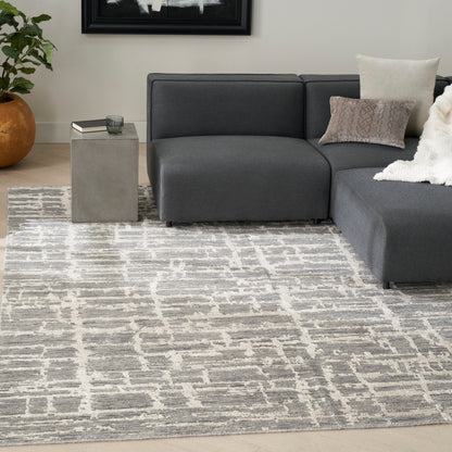 Cream geometric rug in a living room with a charcoal gray sectional with chaise, a concrete cube side table, a plant, a white throw, and beige pillows; 8' x 10'.