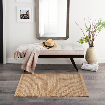 Neutral entryway with tufted white bench, beige throw, straw hat, wood-framed mirror, vase of branches, and jute rug.