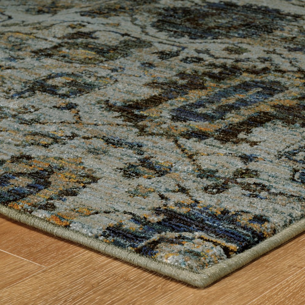 Rectangular area rug with distressed blue, gray and tan patterns, beige binding, on wood floor.