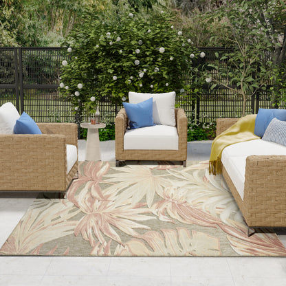 Outdoor wicker seating with white cushions, blue pillows, beige palm-pattern rug, and lush greenery backdrop.