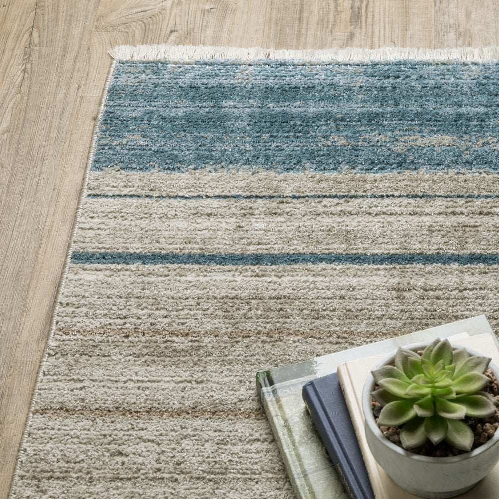 5' x 8' geometric area rug with fringe in blue, dark blue, teal, grey, ivory, beige and tan; power-loomed, stain-resistant.