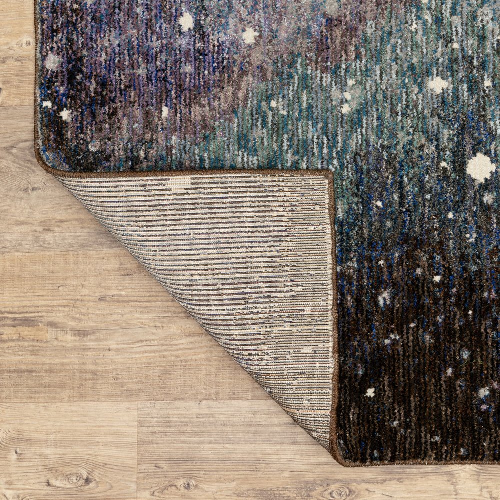 Abstract blue-teal and charcoal runner rug with white specks; corner folded to reveal beige striped underside on wood floor.
