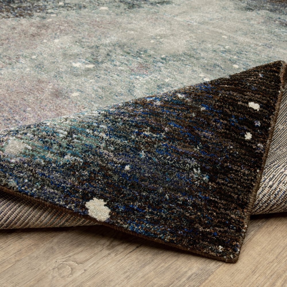 Abstract patterned rug in blue, teal, gray and cream; rolled corner reveals plush pile for a modern living room.