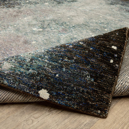 Abstract patterned rug in blue, teal, gray and cream; rolled corner reveals plush pile for a modern living room.