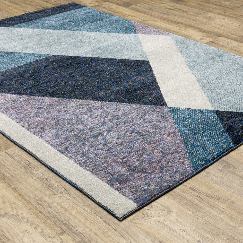 Geometric area rug with blue, navy, grey and cream angled blocks on a wooden floor.