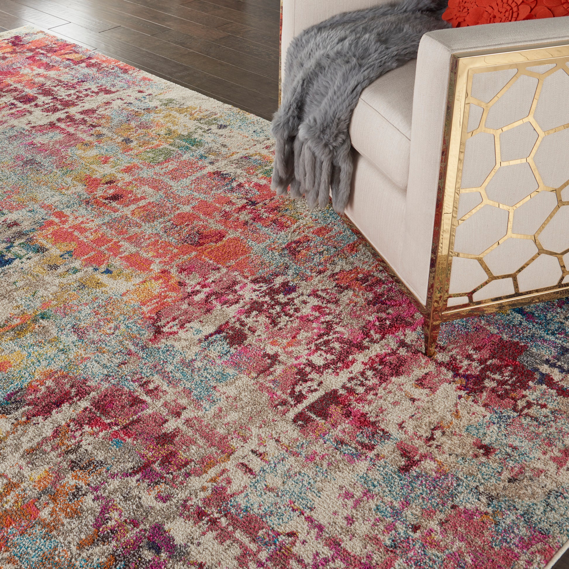 Colorful distressed area rug with abstract floral pattern in reds, blues, yellows; beige sofa with gold honeycomb side table.