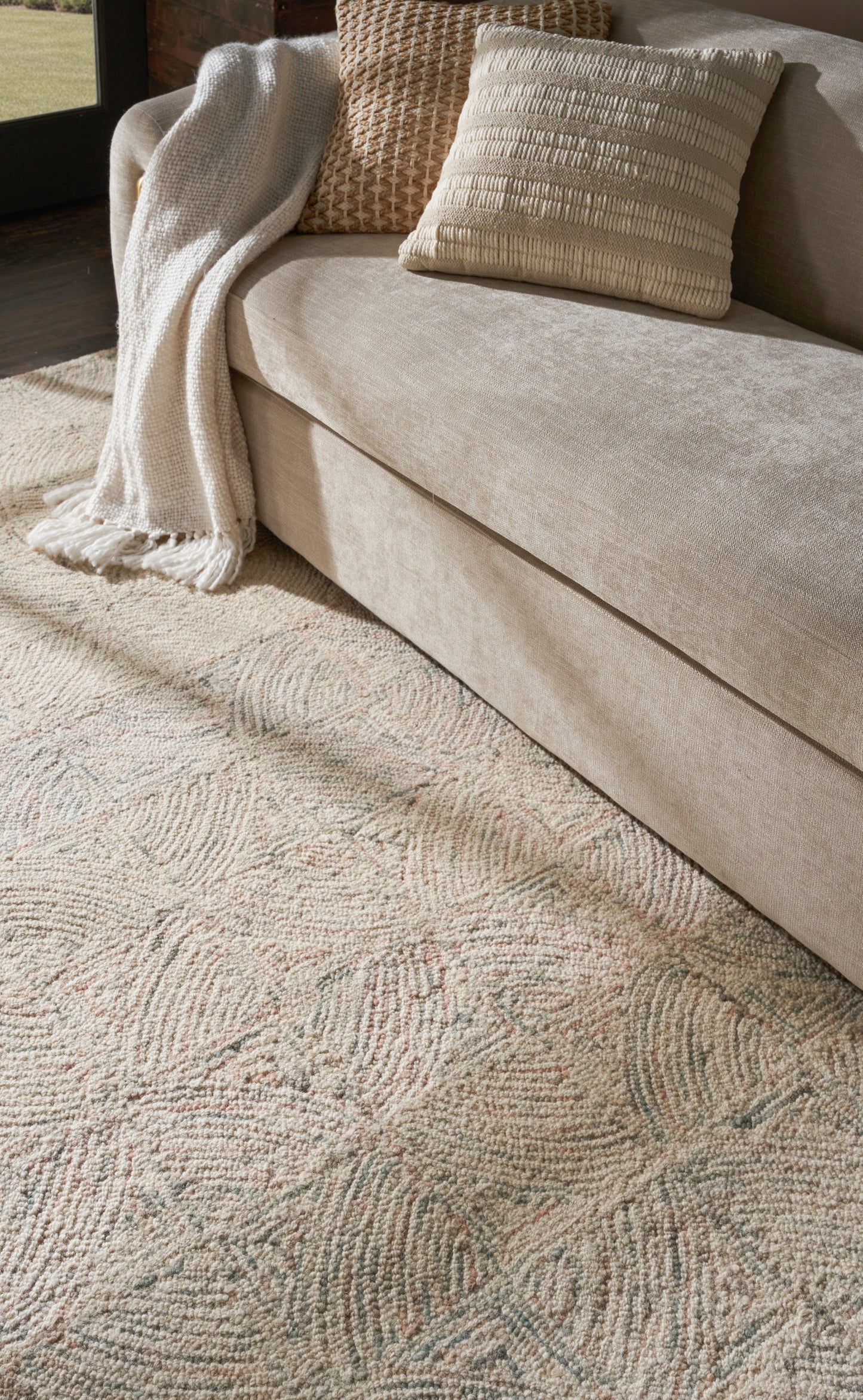 Beige textured area rug in a modern living room, shown under a beige sofa with plush cushions, a cream throw blanket and textured beige pillows.