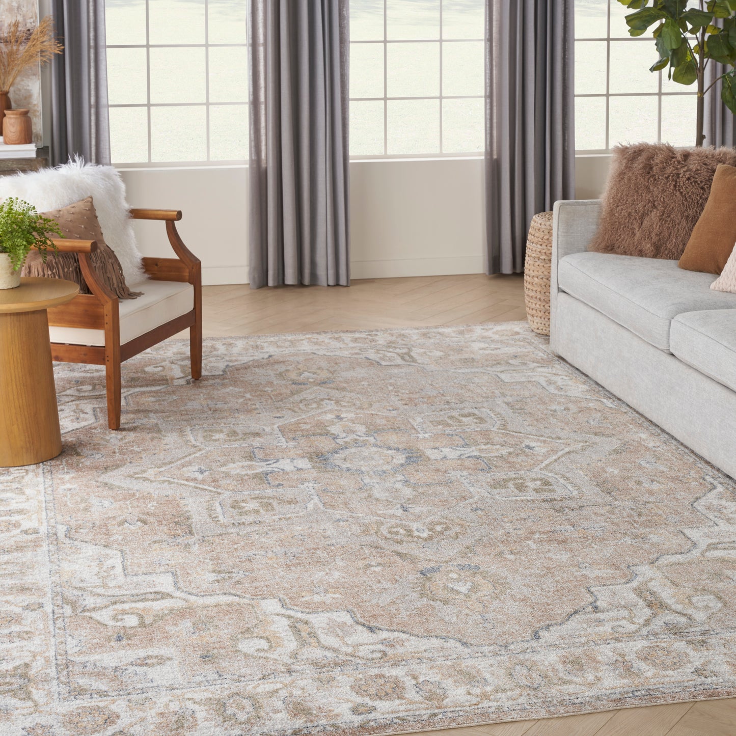 Cozy neutral living room with beige-cream ornate patterned area rug, gray sofa, wooden armchair, wicker side table, and gray curtains.