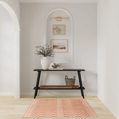 Dark wood console with black legs in an arched entry alcove; vase, framed art, woven basket; peach geometric rug.