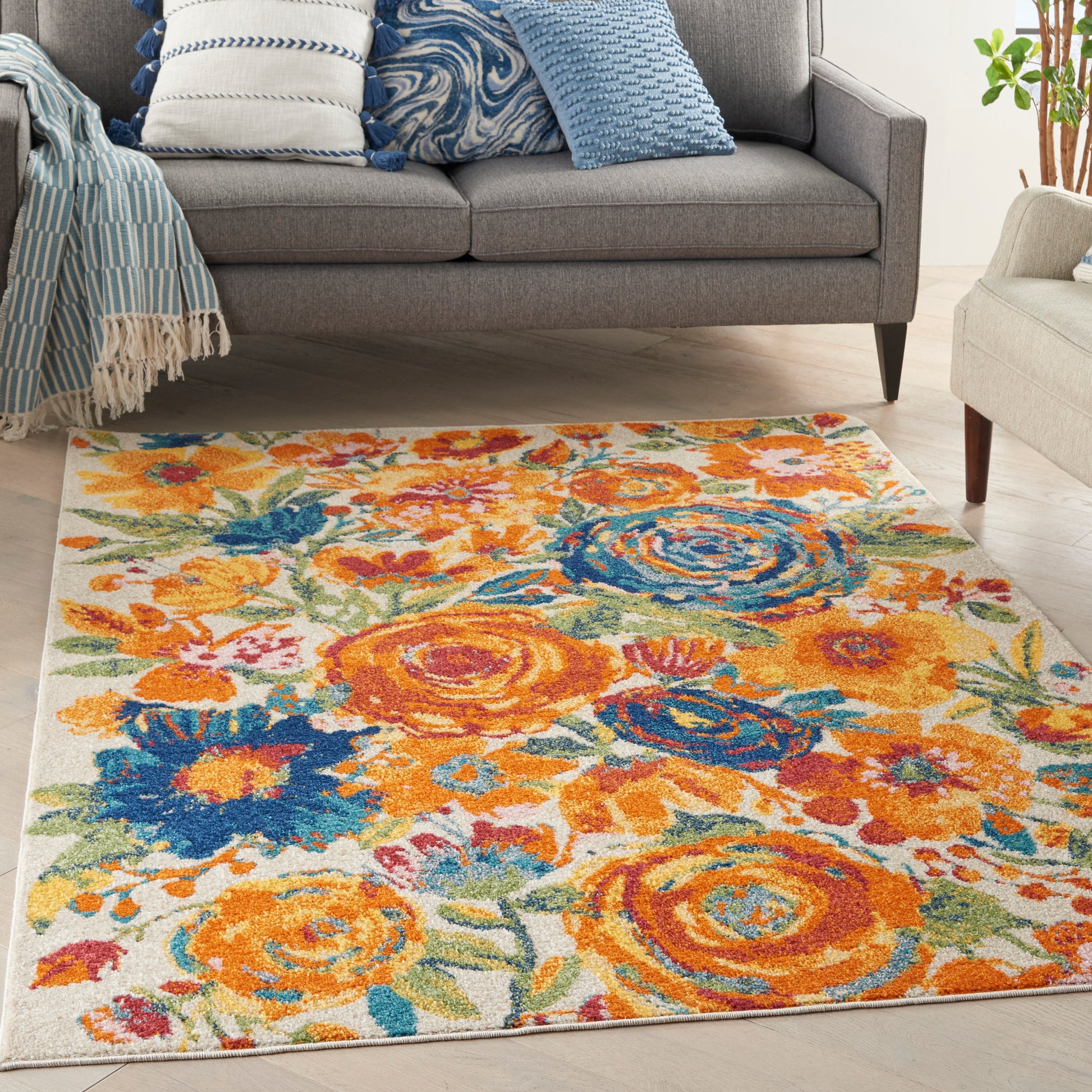 Soft plush floral rug with orange, yellow and blue blooms on a light cream background under a gray sofa.