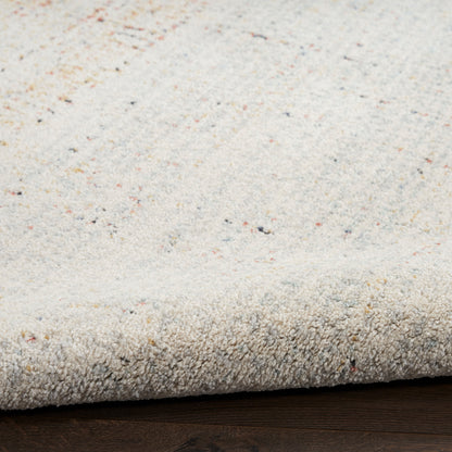 Beige speckled area rug with soft pile; close-up of woven texture and folded edge on dark wood floor.