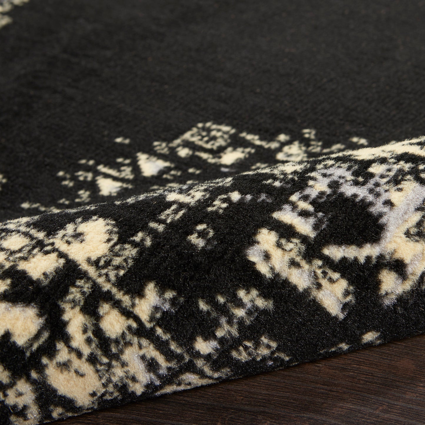Black and ivory Persian-inspired rug with geometric motif, plush pile, folded edge on dark wood floor.
