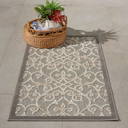 Gray rug with cream scrollwork pattern and dark border; woven texture; round wicker basket with a potted plant on top.