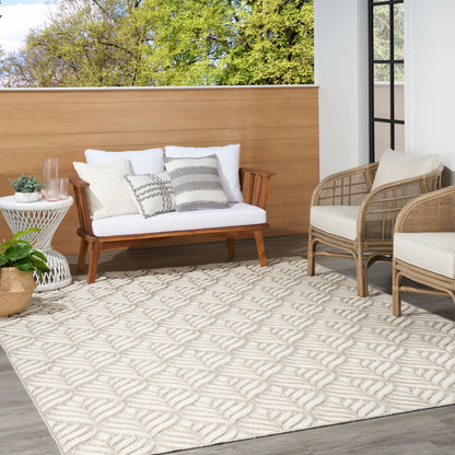 Outdoor lounge: white-cushion wooden sofa, striped pillows, wicker chairs, beige patterned rug, round side table with plants.