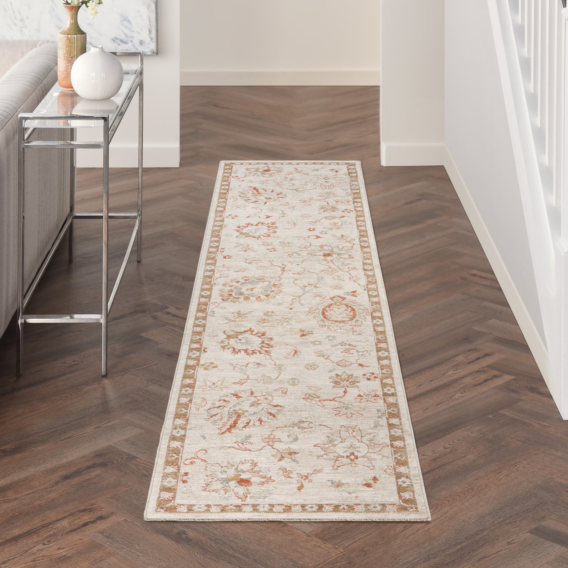 Cream oriental runner rug with beige border and subtle orange floral motifs down a dark herringbone hallway.