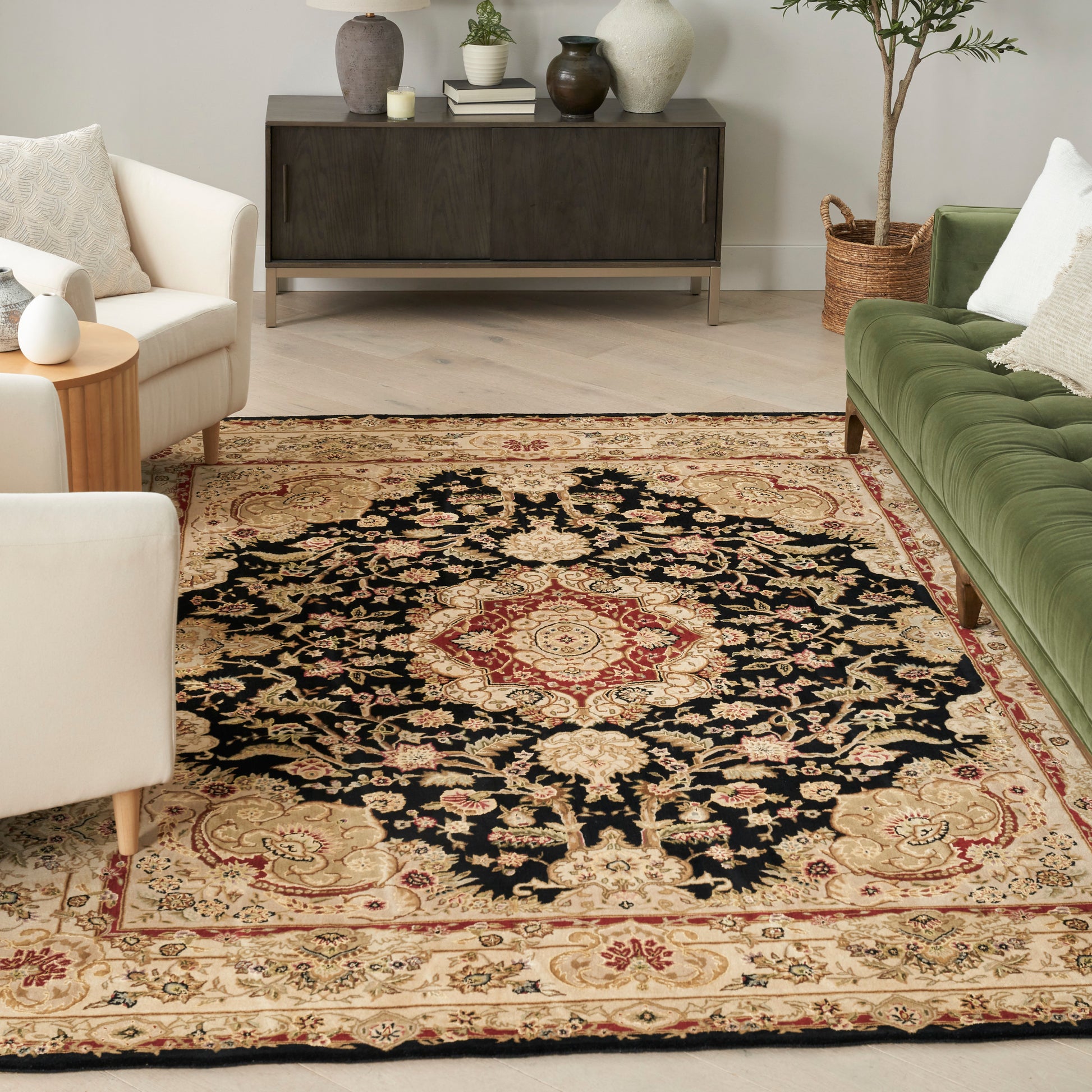 Persian-style rug with black field, red central medallion, beige border; in a living room with cream chairs and a green sofa.