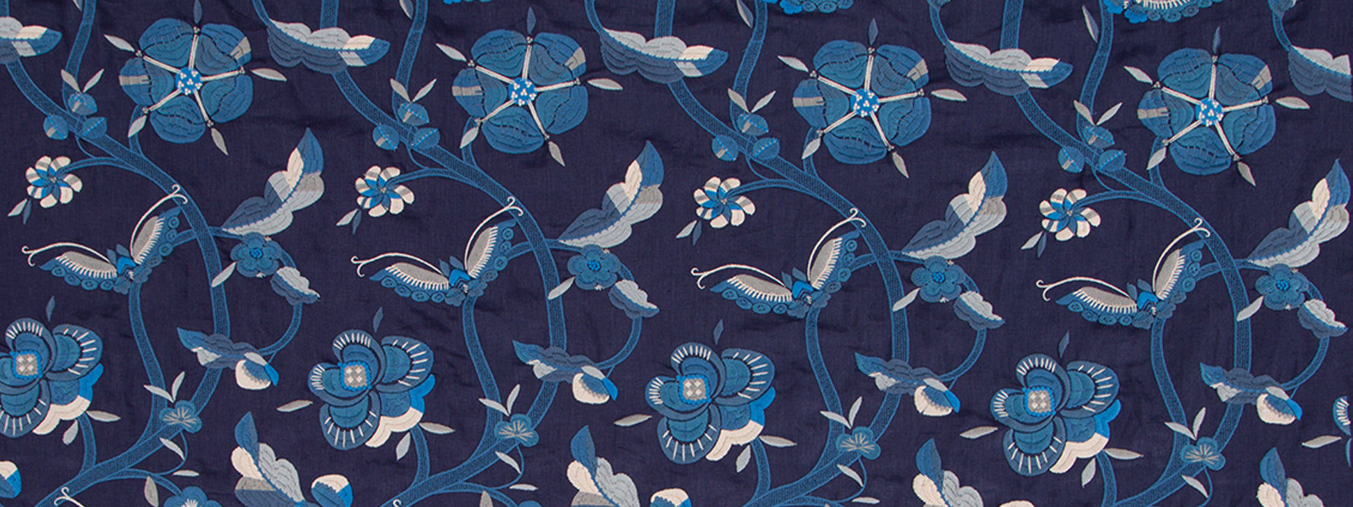 Repeating blue floral print fabric with intertwining vines and blossoms in navy and light blues.