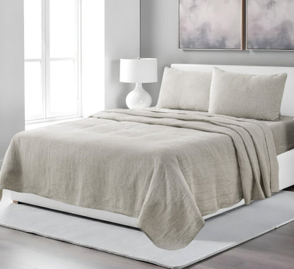 Four piece light gray linen sheet set on a white bed with matching pillowcases.