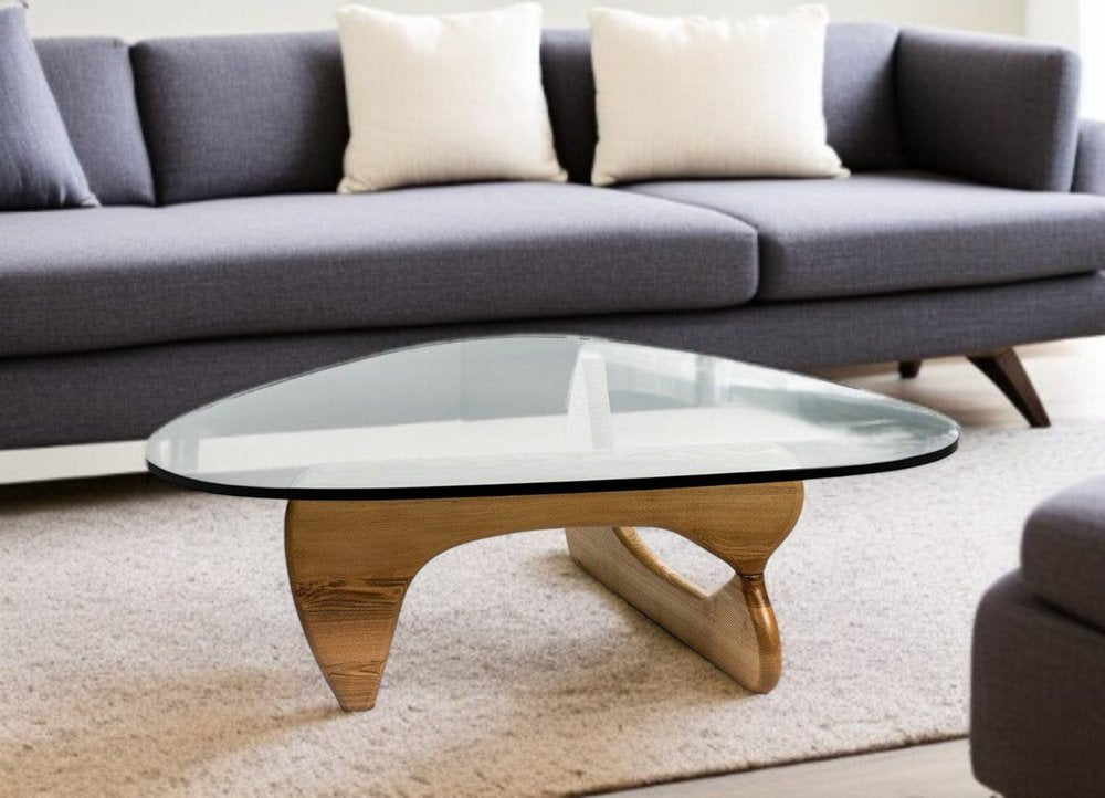 Round glass coffee table with curved wooden sculptural base on a beige rug in a modern living room.
