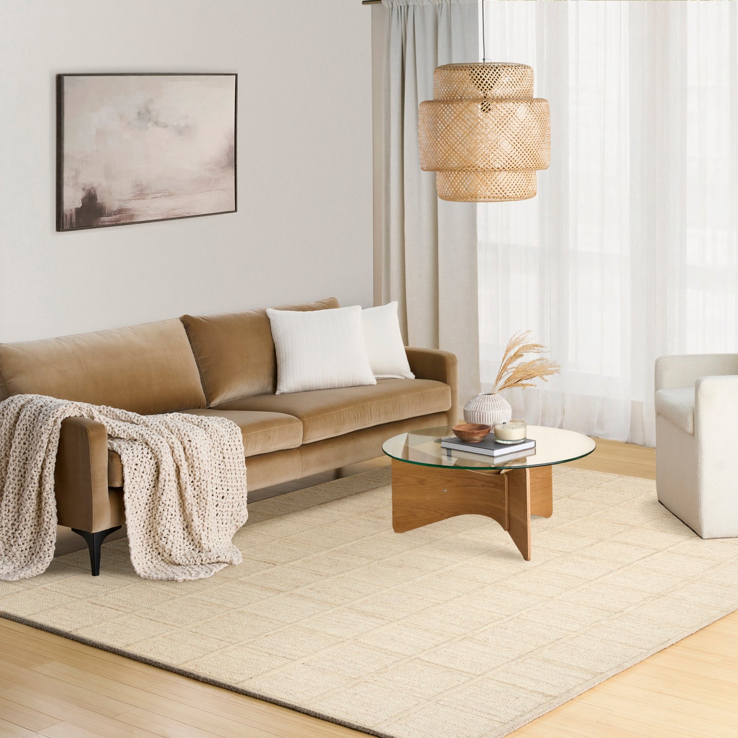 Neutral living room with tan sofa, cream pillows & knit throw; glass coffee table with curved wooden base, woven pendant lamp, beige rug & white armchair.