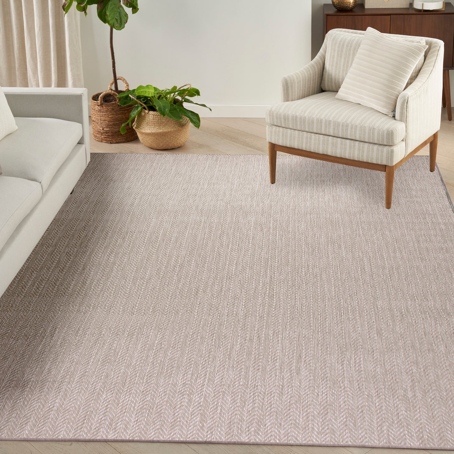 Beige chevron-area rug in a neutral living room with cream sofa, wood-legged armchair, and potted plants.