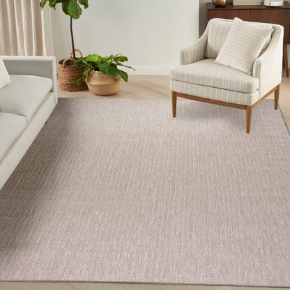 Beige chevron-area rug in a neutral living room with cream sofa, wood-legged armchair, and potted plants.