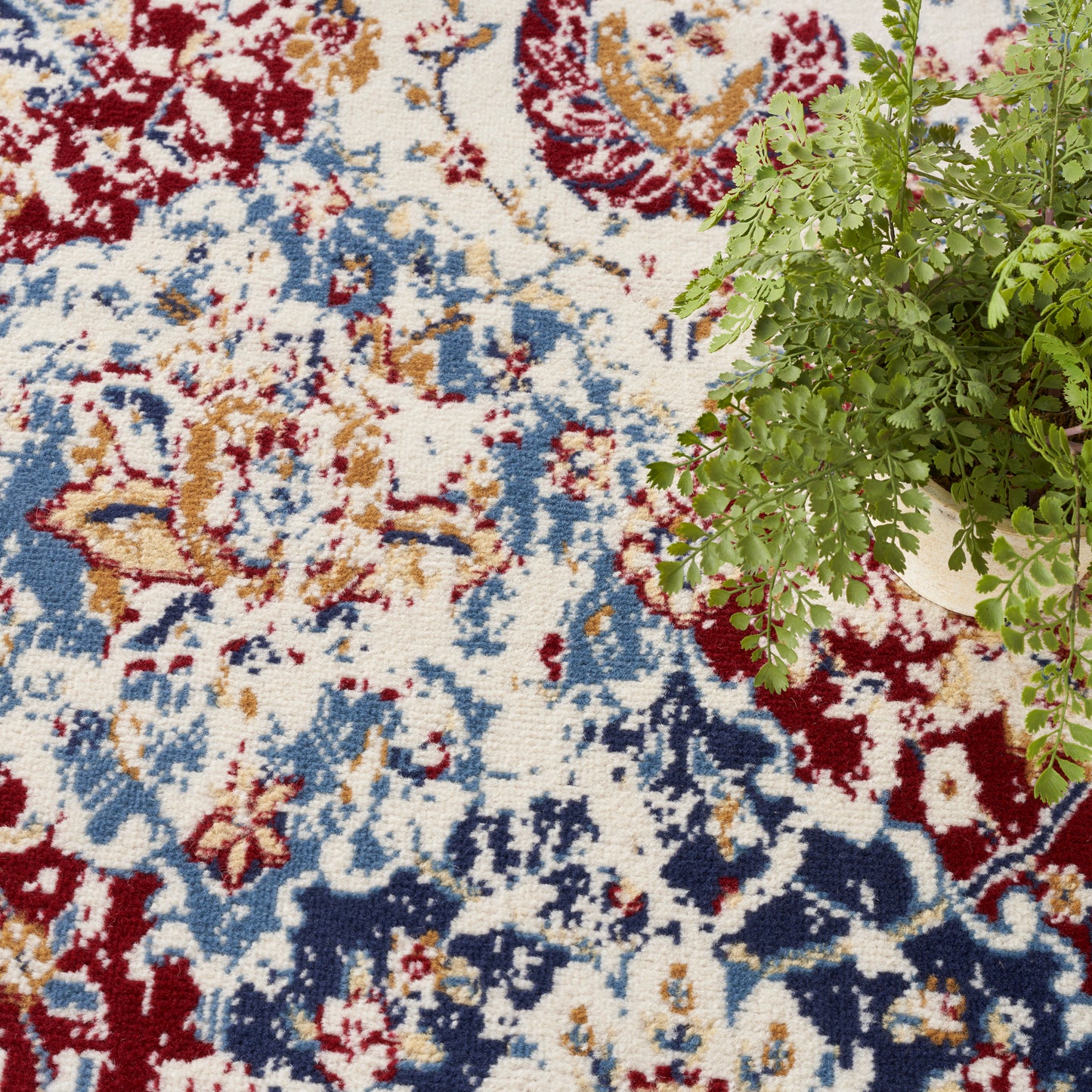 Colorful oriental-style round rug with red, blue, ivory and tan floral motifs; potted fern on the top right.