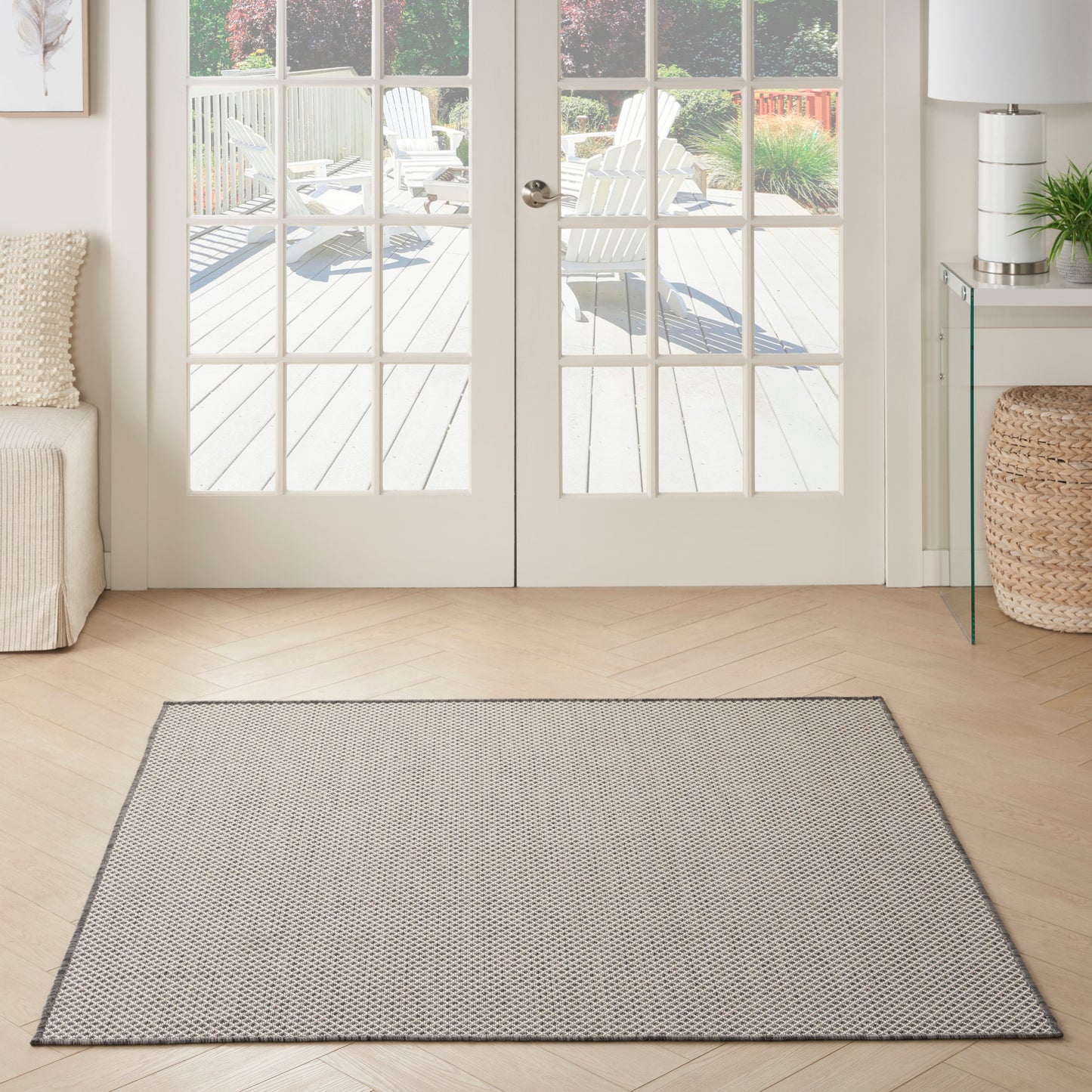 Gray woven square area rug on a light wood floor in a bright living room with glass French doors.