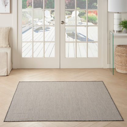 Gray woven square area rug on a light wood floor in a bright living room with glass French doors.