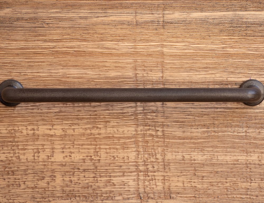 Dark bronze metal towel bar with round end mounts on wood surface, industrial rustic style.