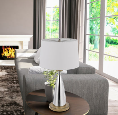 Brown metal geometric USB table lamp with a white empire shade on a round wood table in a bright living room.