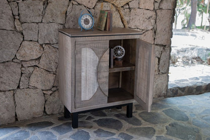 Rustic wood cabinet with circular cut-out panel doors, open inner shelf, black legs; blue clock and books on top.