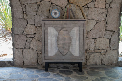 Graywashed wooden cabinet with woven cane doors on black legs, set on a stone patio with a clock on top.