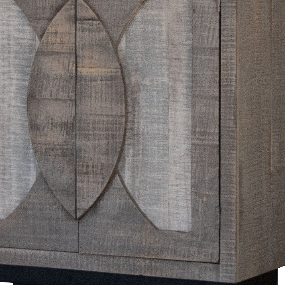 Graywashed wooden cabinet with carved leaf motif on panel doors; rustic farmhouse storage.