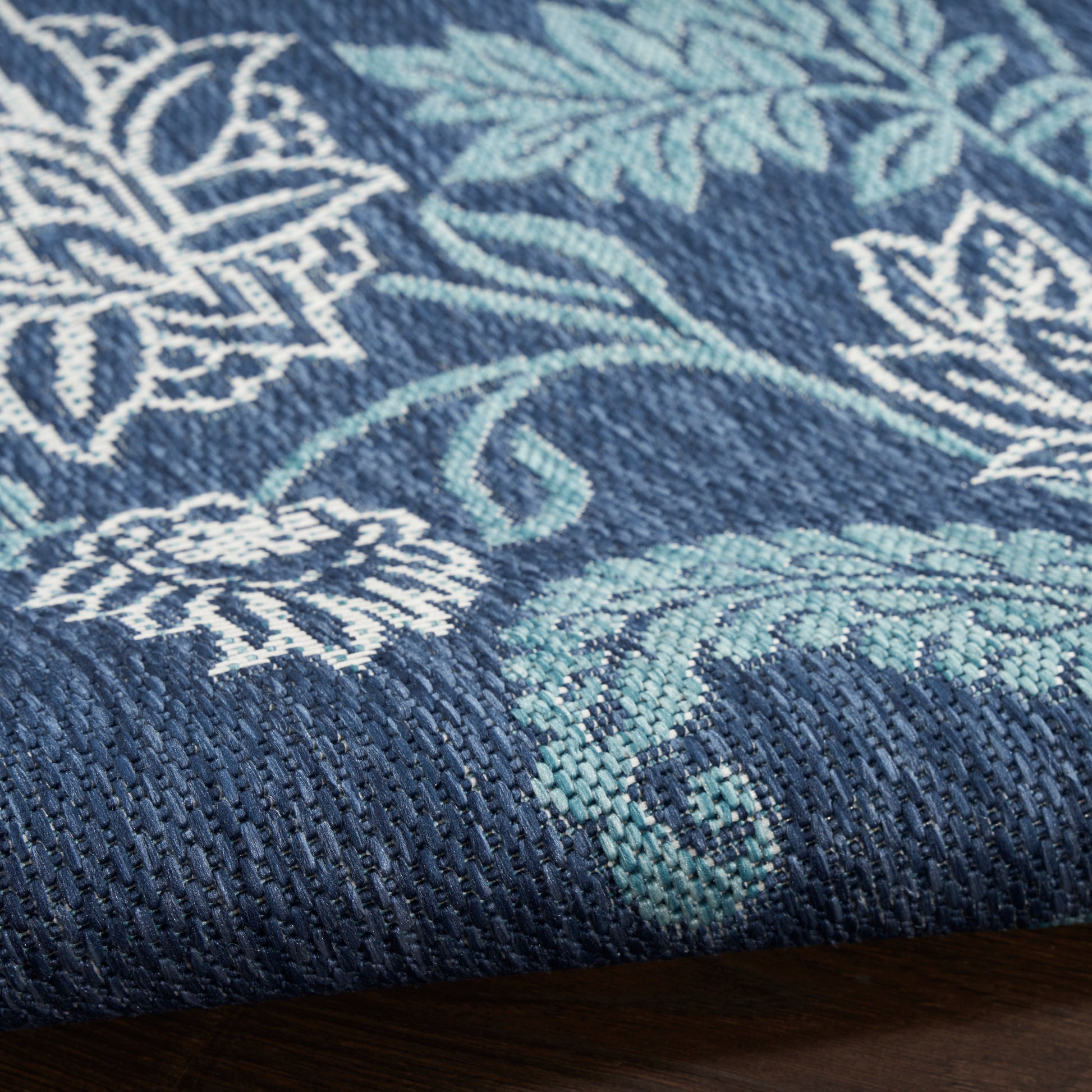 Navy blue woven rug with teal and white botanical pattern; textured weave and visible edge.