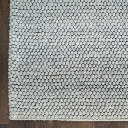 Close-up of a light gray loop-pile rug with pebble-like texture, edge visible on dark wood floor.