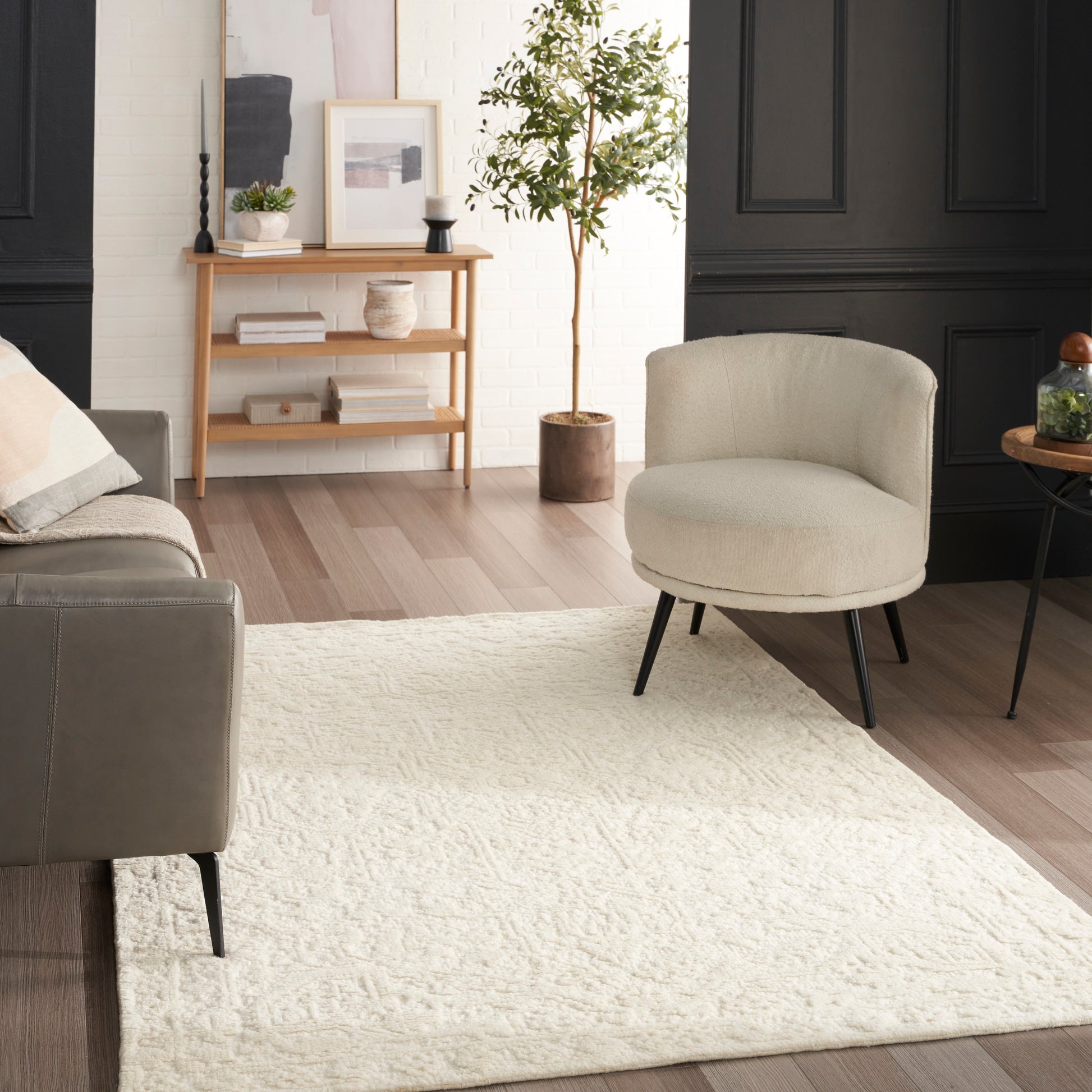 Cream round upholstered lounge chair with gray sofa, white textured rug, wood floors, and black-paneled walls.