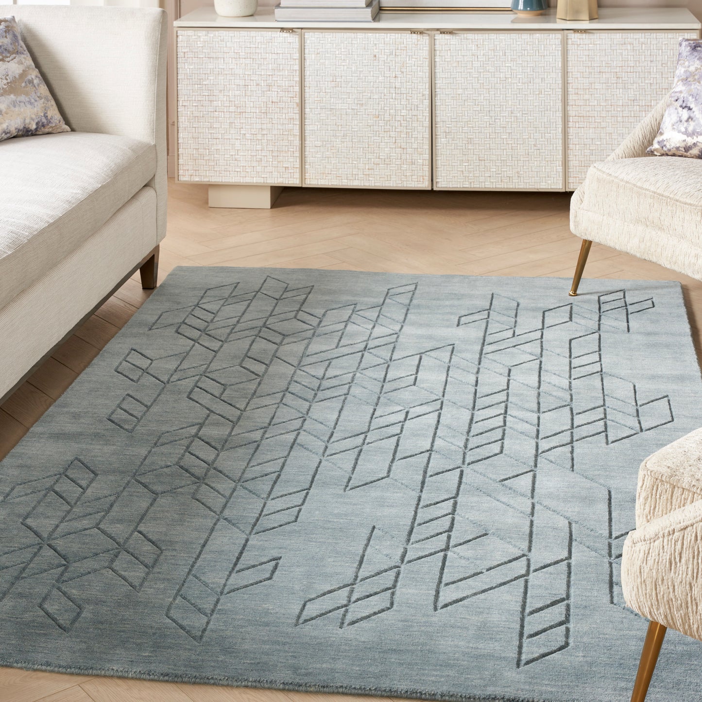 Grey-blue area rug with geometric diamond pattern in a modern living room; light sofas and a woven cabinet.