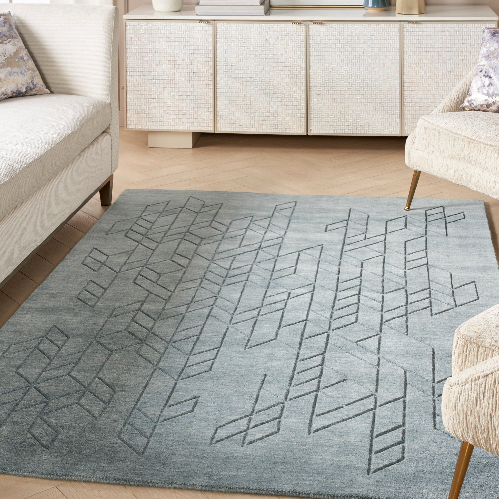 Grey-blue area rug with geometric diamond pattern in a modern living room; light sofas and a woven cabinet.