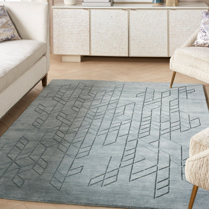 Grey-blue area rug with geometric diamond pattern in a modern living room; light sofas and a woven cabinet.